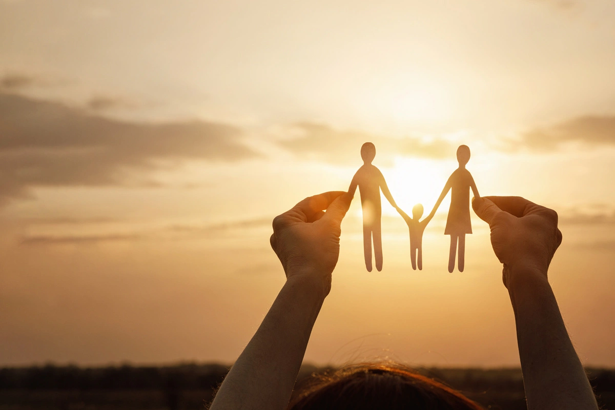 Mains tenant des silhouettes en papier d'une famille devant un coucher de soleil, représentant l'adoption avec l'aide d'un avocat.