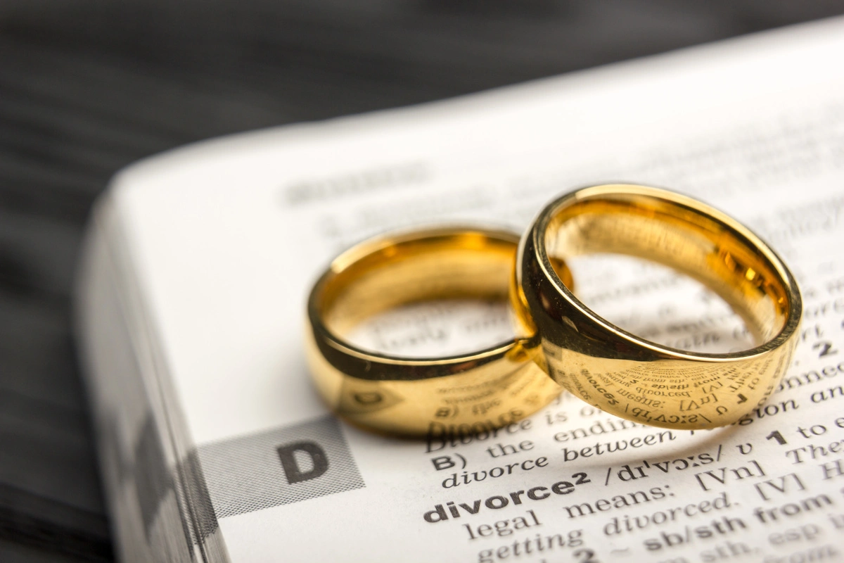 Deux alliances en or posées sur une page de dictionnaire ouverte à la définition du divorce.